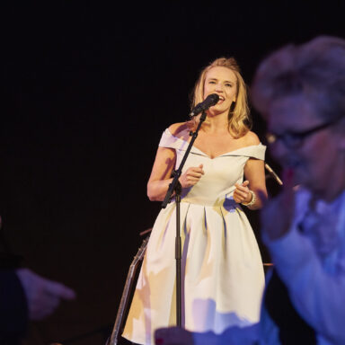 Sängerin im hellblauen Petticoat mit glücklichen Tänzerinnen vor der Bühne