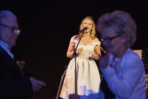 Sängerin im hellblauen Petticoat mit glücklichen Tänzerinnen vor der Bühne