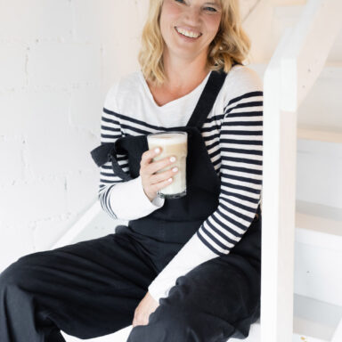 Jutta Mesch llachend auf der Treppe sitzend mit einer Latte Macchiato in der Hand.