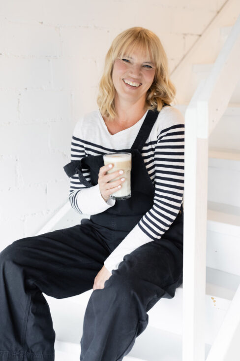 Jutta Mesch llachend auf der Treppe sitzend mit einer Latte Macchiato in der Hand.
