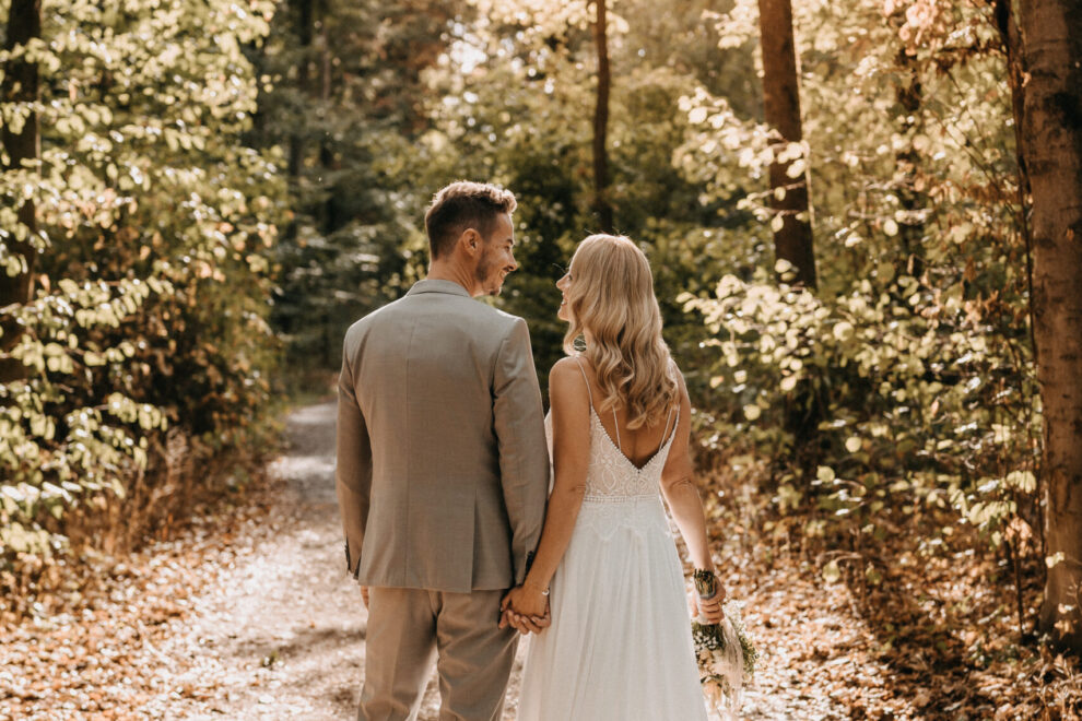Hochzeitsfotoshooting, Brautpaar mit Blick in den Wald mit Rückenansicht