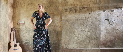 Jutta Mesch I tanzend vor einer Wand im Industrial Look mit Gitarre in der Ecke angelehnt