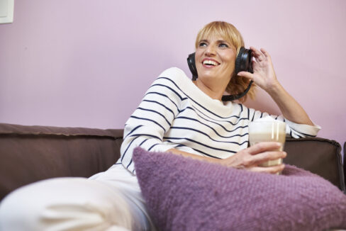 Blonde Frau mit Kopfhörer sitzend auf einem Sofa in pink, lila Tönen