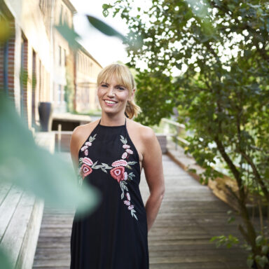 Blonde Frau mit Zopf schaut lächelnd in die Kamera