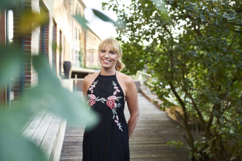 Blonde Frau mit Zopf schaut lächelnd in die Kamera